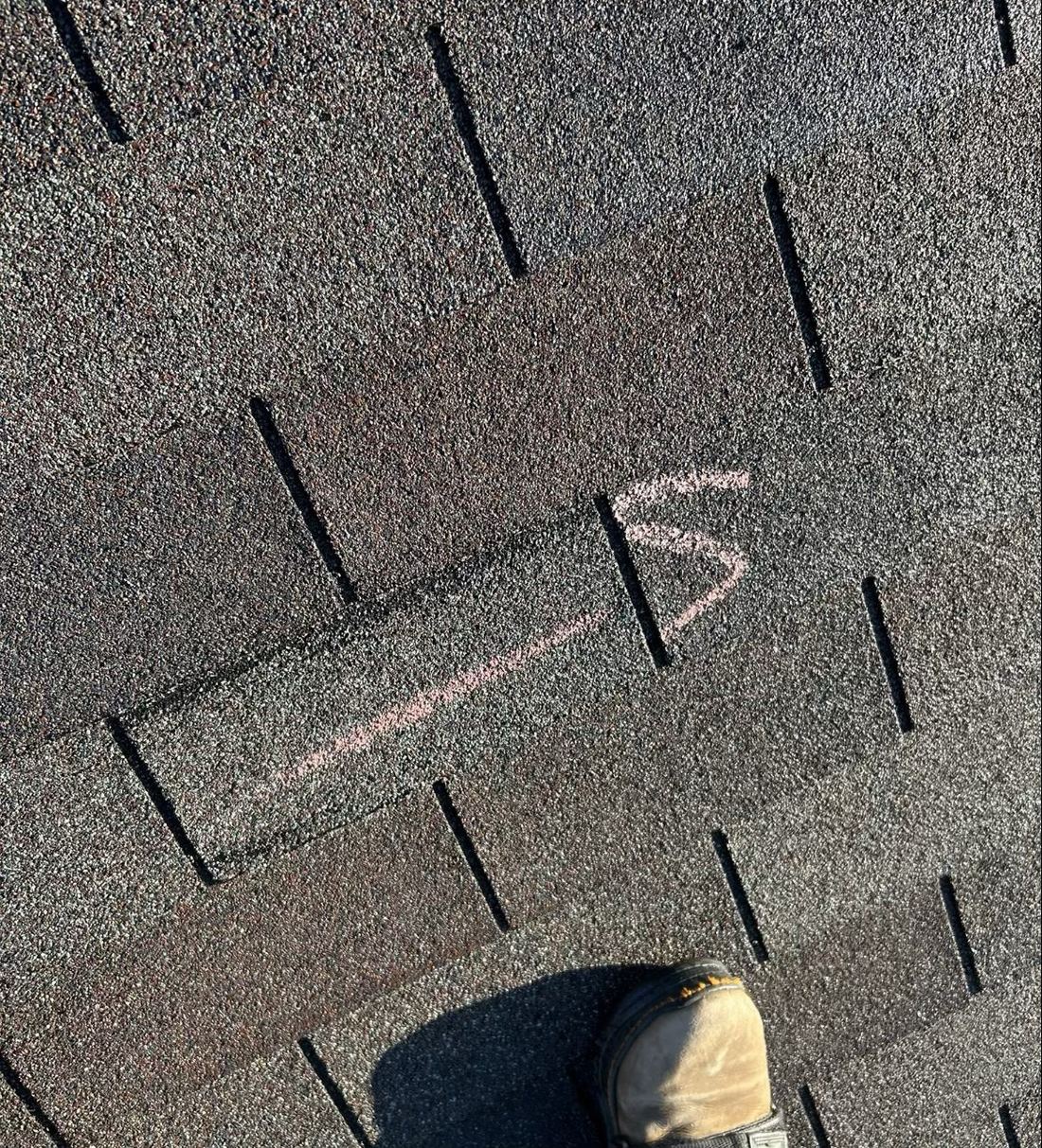 A 3-tab shingle with a fold line along the top and the left corner lifted where the seal was broken