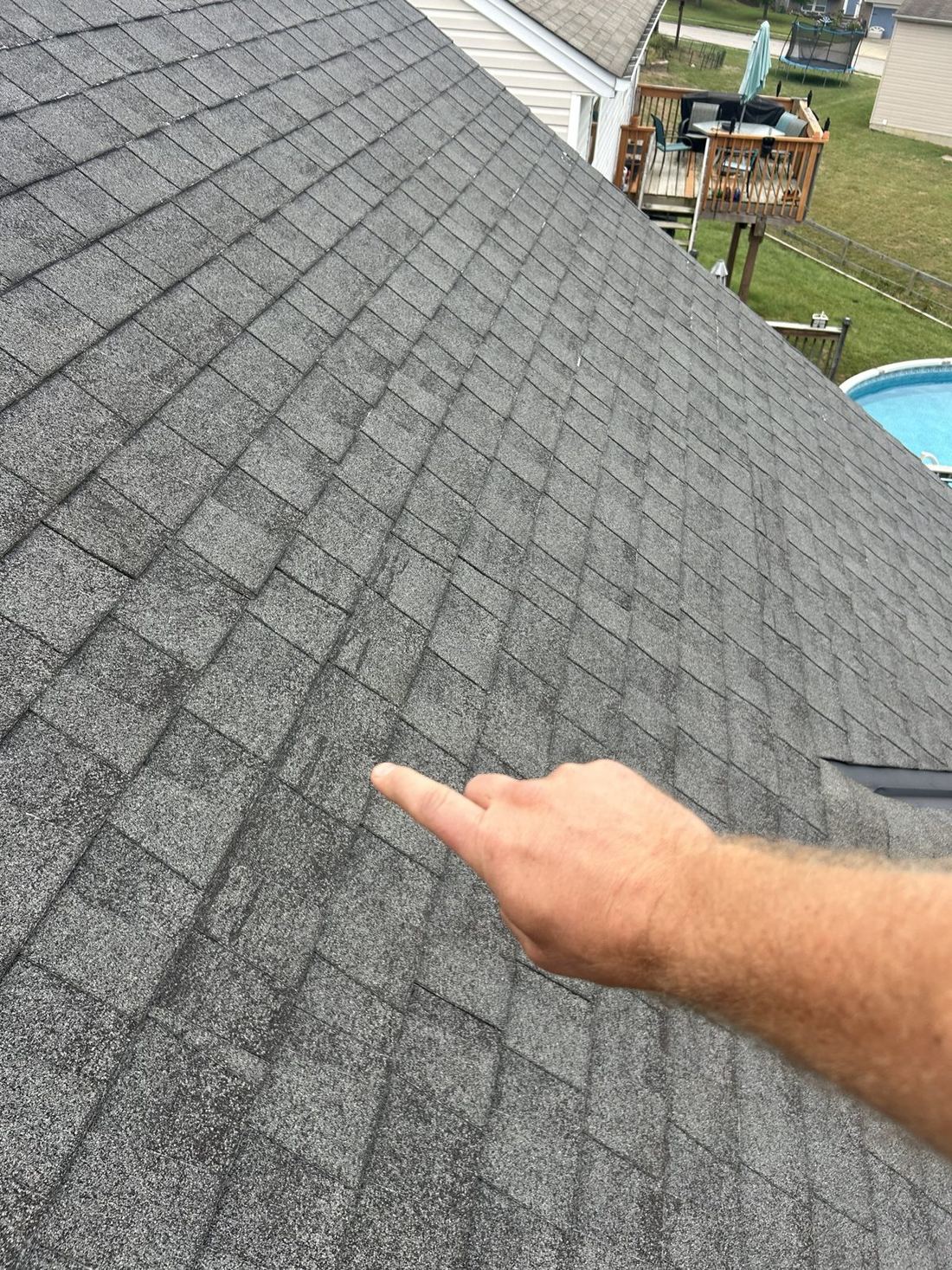 A dimensional shingle roof with scuffed patches near a roof vent, pointed out by an inspector