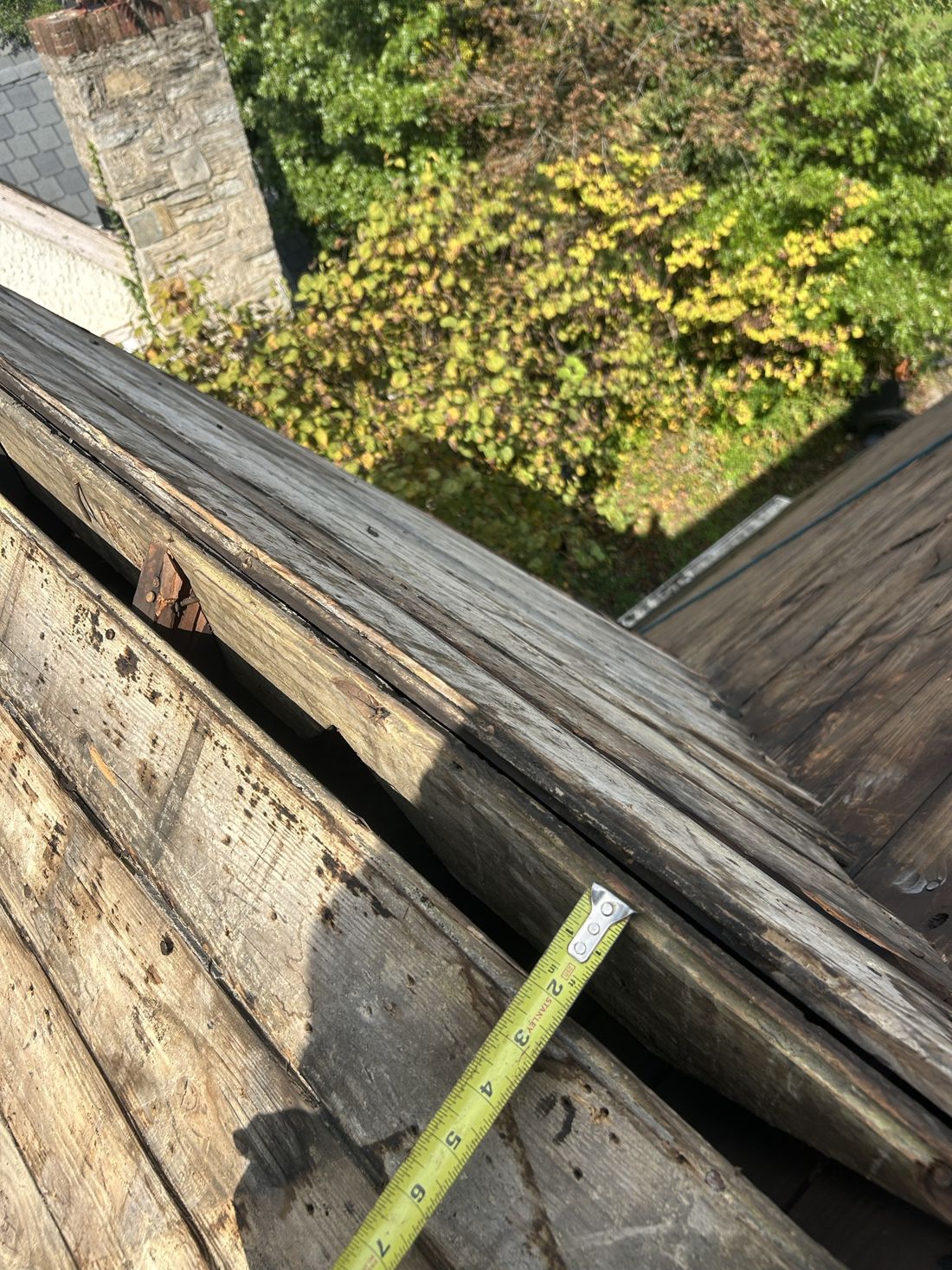 Old plank roof decking exposed during tear-off, with split and separated boards and a tape measure for scale