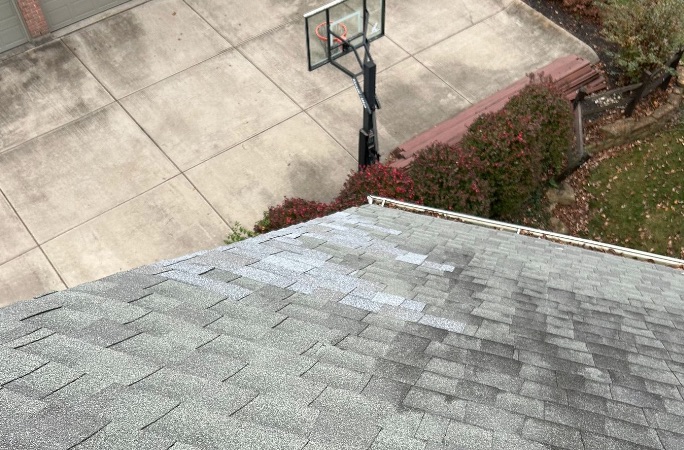 A roof slope showing a section of light-colored replacement shingles against the darker weathered shingles around them