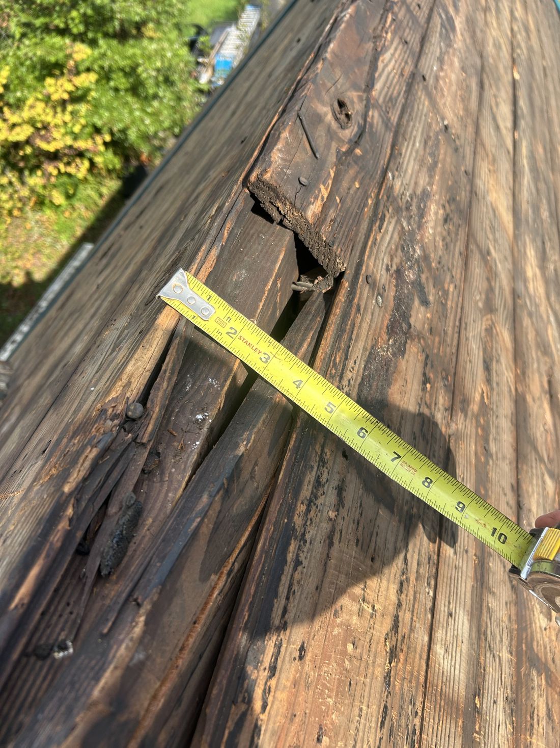 A rotted roof decking plank broken apart at tear-off, leaving a hole down to the rafter