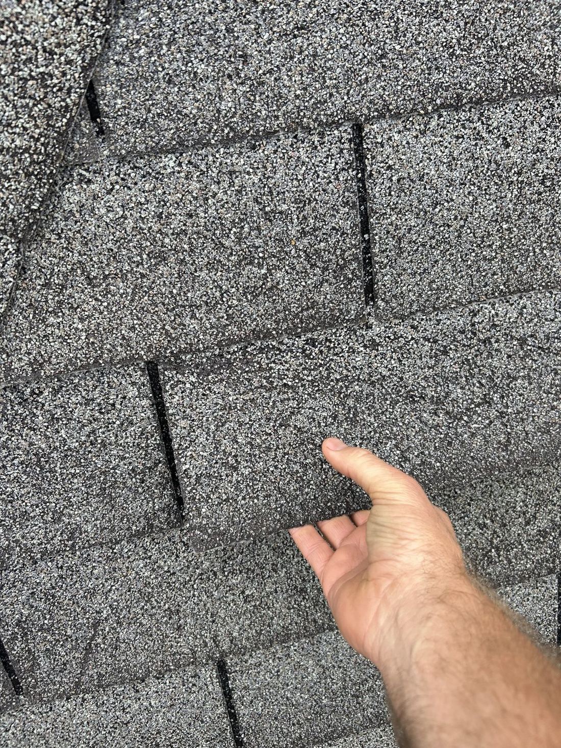 A 3-tab shingle tab lifted by hand with no resistance, showing a broken seal from wind