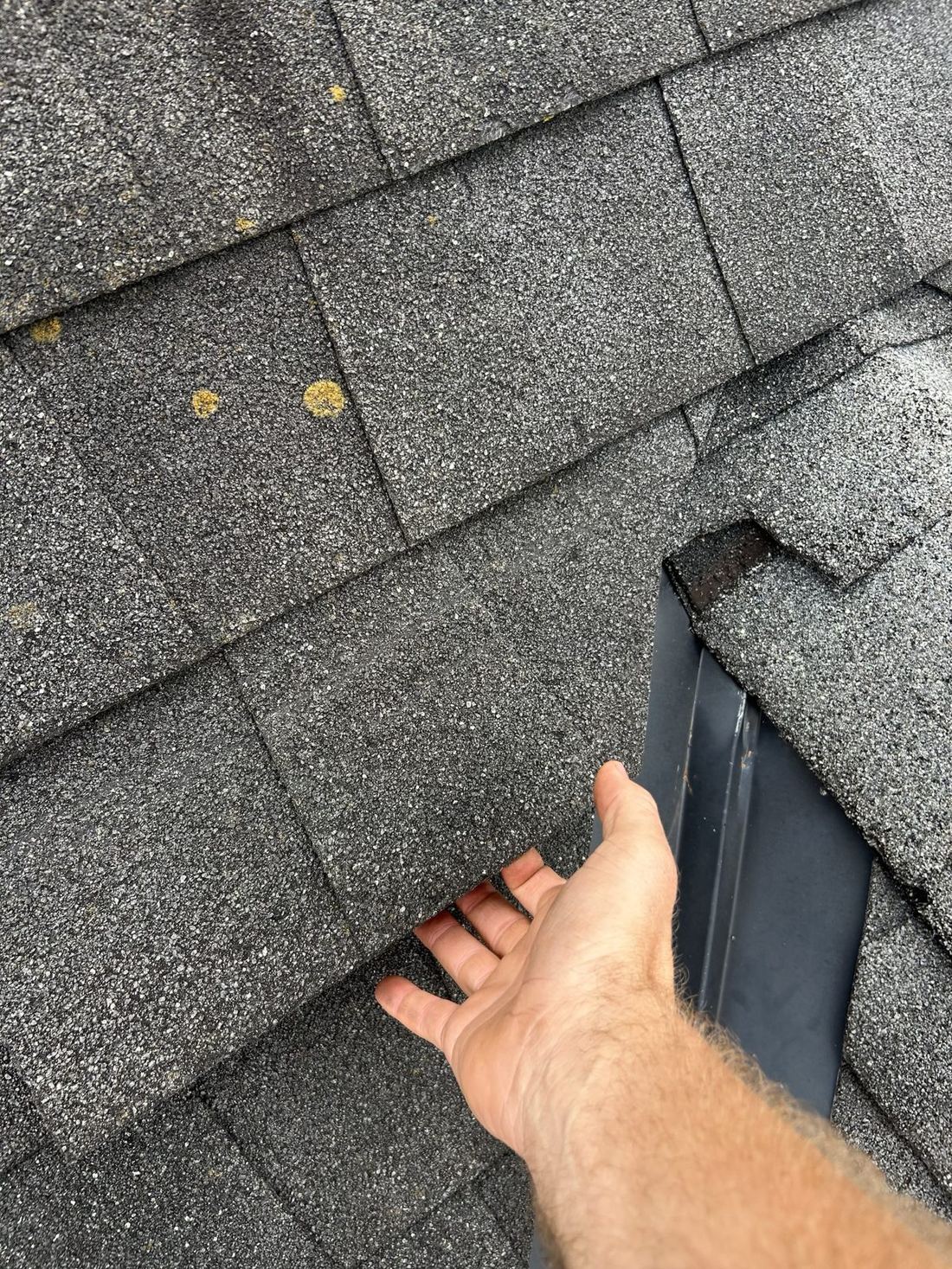 A dimensional shingle lifted by hand along the cut edge next to a metal valley